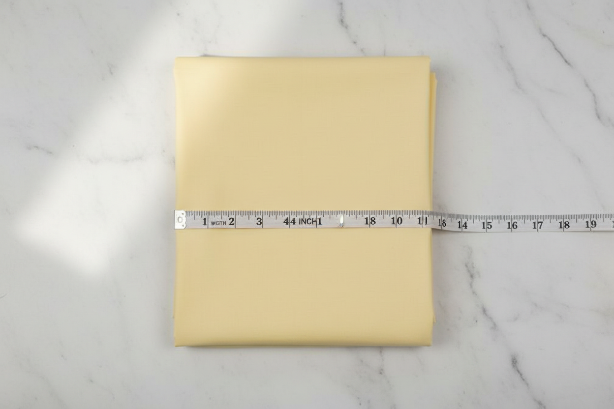 Flat lay of Lemon Cotton Poplin Fabric with measuring tape showing 44 inch width
